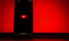 A phone showing the YouTube logo stands propped in front of a glowing red laptop.