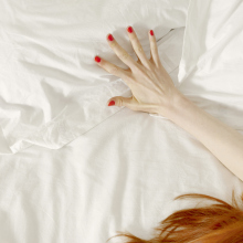 A woman's hand outstretched on white bedsheets, her red hair visible in the bottom corner of the photo. 