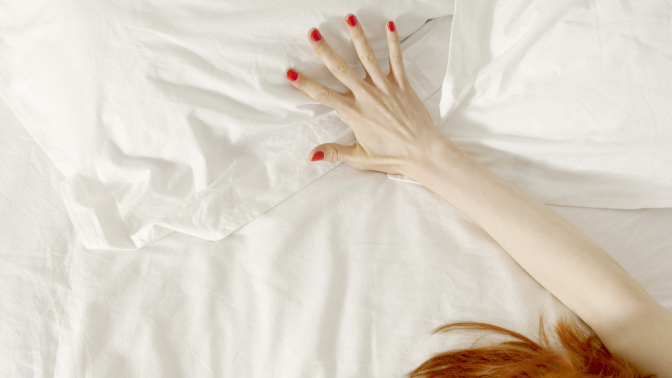 A woman's hand outstretched on white bedsheets, her red hair visible in the bottom corner of the photo. 
