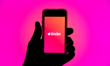 Tinder app seen displayed on a smartphone screen in front of pink background