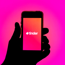 Tinder app seen displayed on a smartphone screen in front of pink background