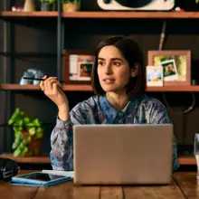 A person at a desk with a notebook computer and a pen.