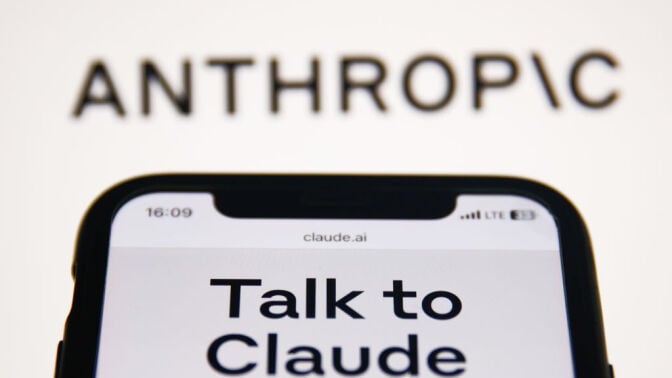 Anthropic Claude website displayed on a phone screen and Anthropic logo displayed on a screen in the background