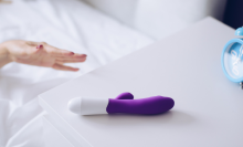 Young woman holding sex toy dildo vibrator in bed