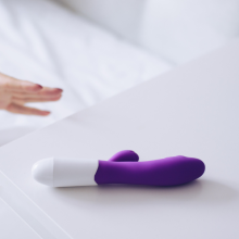 Young woman holding sex toy dildo vibrator in bed