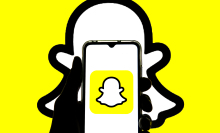 A hand holding a smartphone with the Snapchat logo visible. 