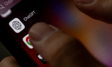 A finger points to the ChatGPT app on a phone screen.