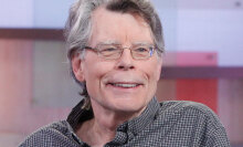 Stephen King wearing a shirt and grinning while looking at someone off-camera.