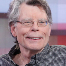 Stephen King wearing a shirt and grinning while looking at someone off-camera.