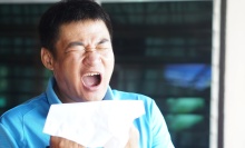 Man in a blue shirt sneezing while holding a tissue