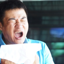 Man in a blue shirt sneezing while holding a tissue