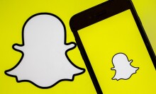 A photo shows the logo of 'Snapchat' app on a screen of a smart phone and replicated on a yellow background.