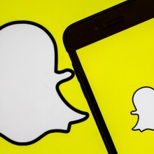 A photo shows the logo of 'Snapchat' app on a screen of a smart phone and replicated on a yellow background.