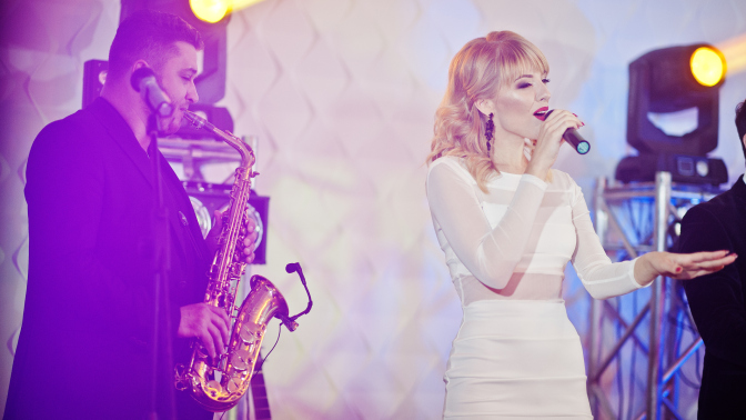 woman singing on stage with a man playing the trombone