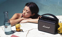 Woman lounging in pool with Marshall speaker and drinks by her side