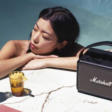 Woman lounging in pool with Marshall speaker and drinks by her side