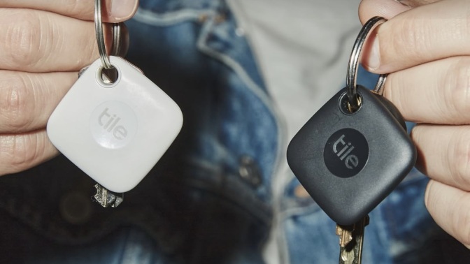 person holding a key in each hand with black and white tile tracker on key rings