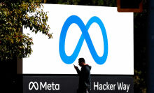 A pedestrian walks in front of a new logo and the name 'Meta' on the sign in front of Facebook headquarters.