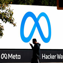 A pedestrian walks in front of a new logo and the name 'Meta' on the sign in front of Facebook headquarters.