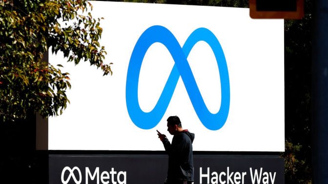 A pedestrian walks in front of a new logo and the name 'Meta' on the sign in front of Facebook headquarters.