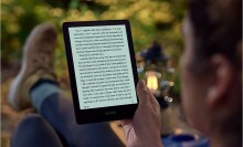 a person reads an amazon kindle e-reader while sitting outdoors. they're wearing workout pants and hiking boots.