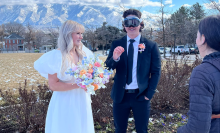 woman in white wedding gown next to groom with apple vision pro headset on, with wedding photographer on far right