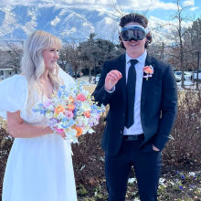 woman in white wedding gown next to groom with apple vision pro headset on, with wedding photographer on far right