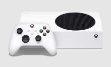 an xbox wireless controller leaning up against an xbox series s on a gray background