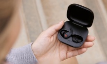 person sitting down outside holding open black beats fit pro case with earbuds inside