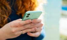 Woman with red hair holds an iPhone with a blue-green case on it. 