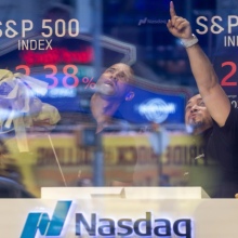 Two men at the NASDAQ stock exchange point at falling numbers on a screen. 