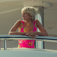 Elizabeth Debicki as Princess Diana in "The Crown" standing on a luxury yacht in a pink swimsuit.