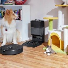 A Roborock robot vacuum cleans up pet hair in a playroom next to a dog
