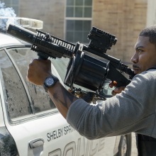 Terry Richmond fires a gun over a cop car.