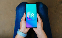 ios 18 logo on a smartphone being held in someone's hands on their lap