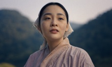 A close-up of young Sunja in the Japanese countryside, with large forested hills behind her.