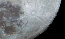 The International Space Station flies in front of the surface of the moon. 