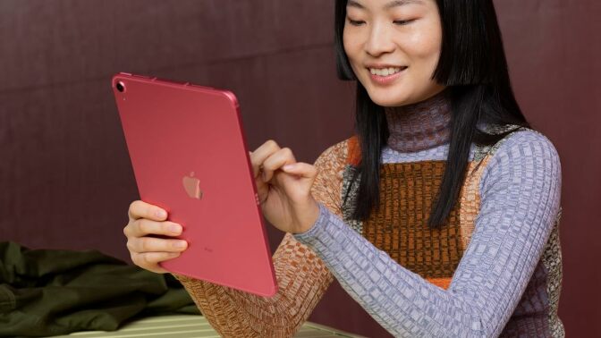 a person with long black hair sits at a table while using a red apple ipad