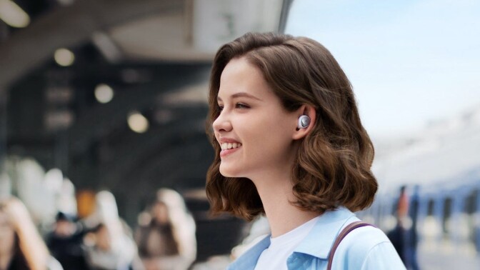 a person stands in near others while outside with the anker soundcore space a40 earbuds in her ears