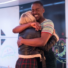 The Doctor and Ruby Sunday share a hug in a corridor with baby art on the walls.