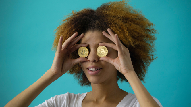 Person holding two gold bitcoins over her eyes