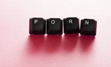 Four keys from a computer keyboard, spelling out the word "porn". A light pink backdrop behind. 