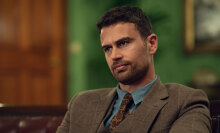 A man in a suit sits in a chair indoors.