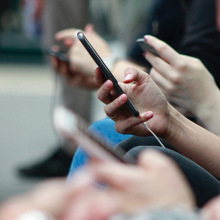 Hand using phone in focus with other hands and phones in fore- and background blurred