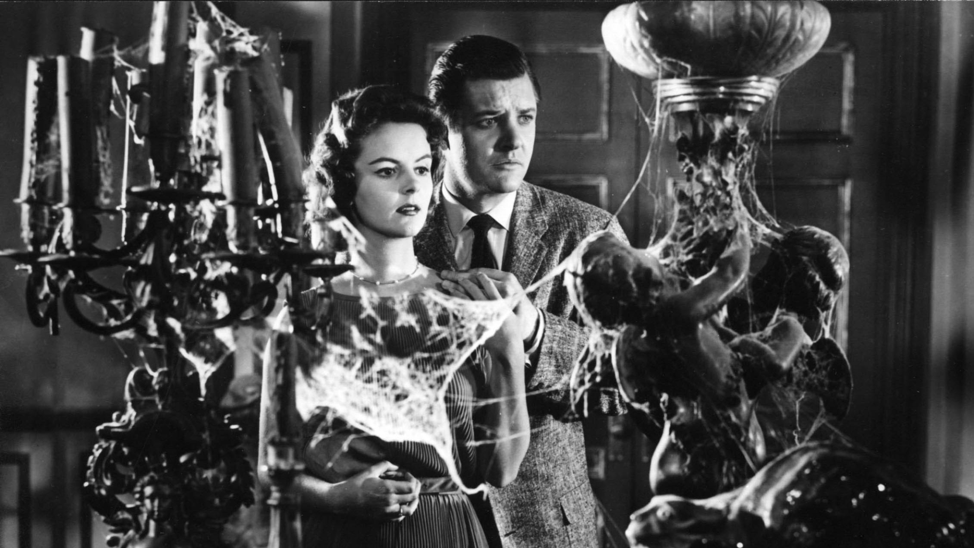 A man and woman stand looking at old lamps covered in cobwebs.