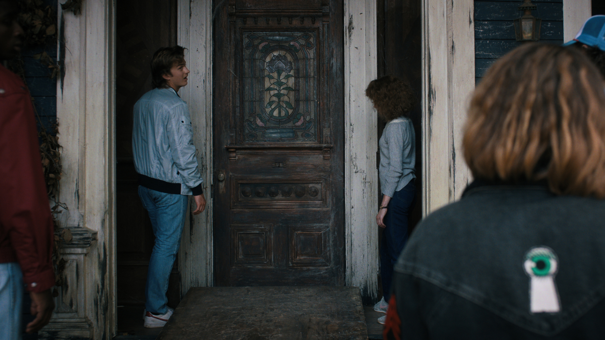 People stand outside a creepy old house's door.