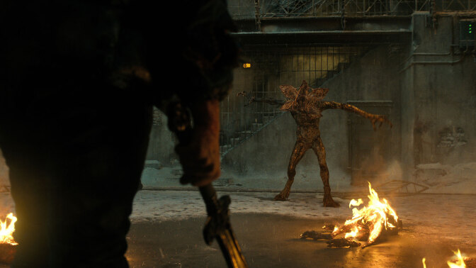 A man with a sword faces off against a monster in an empty prison.