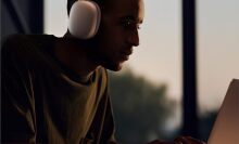 A man wears Apple AirPods Max while sitting in front of a laptop