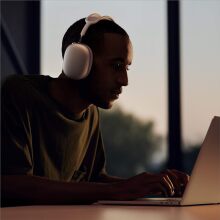 A man wears Apple AirPods Max while sitting in front of a laptop