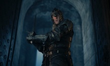 Daemon Targaryen walks through a large doorway in Harrenhal, holding a sword and wearing full armor.